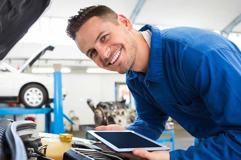 Smiling technician servicing a car engine while holding a tablet